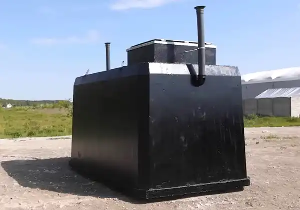 Large black rectangular industrial storage tank with two vertical vents, outdoors on a dirt lot.