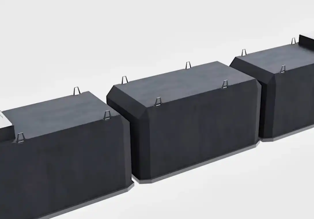 Row of large black industrial storage blocks with lifting handles on top, viewed from an angled perspective.